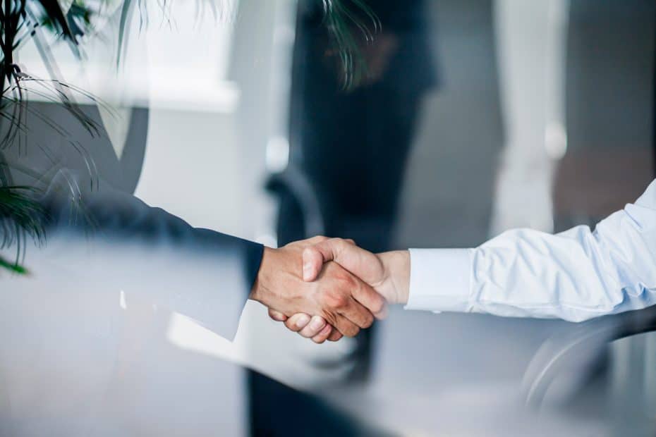 Zwei Menschen in Business Hemd schütteln sich die Hände.